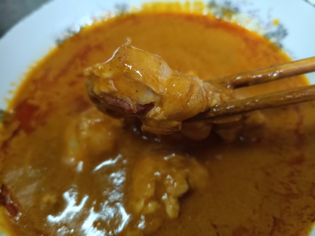 鶏手羽元入りバターチキンカレーの手羽元を箸ですくっている画像