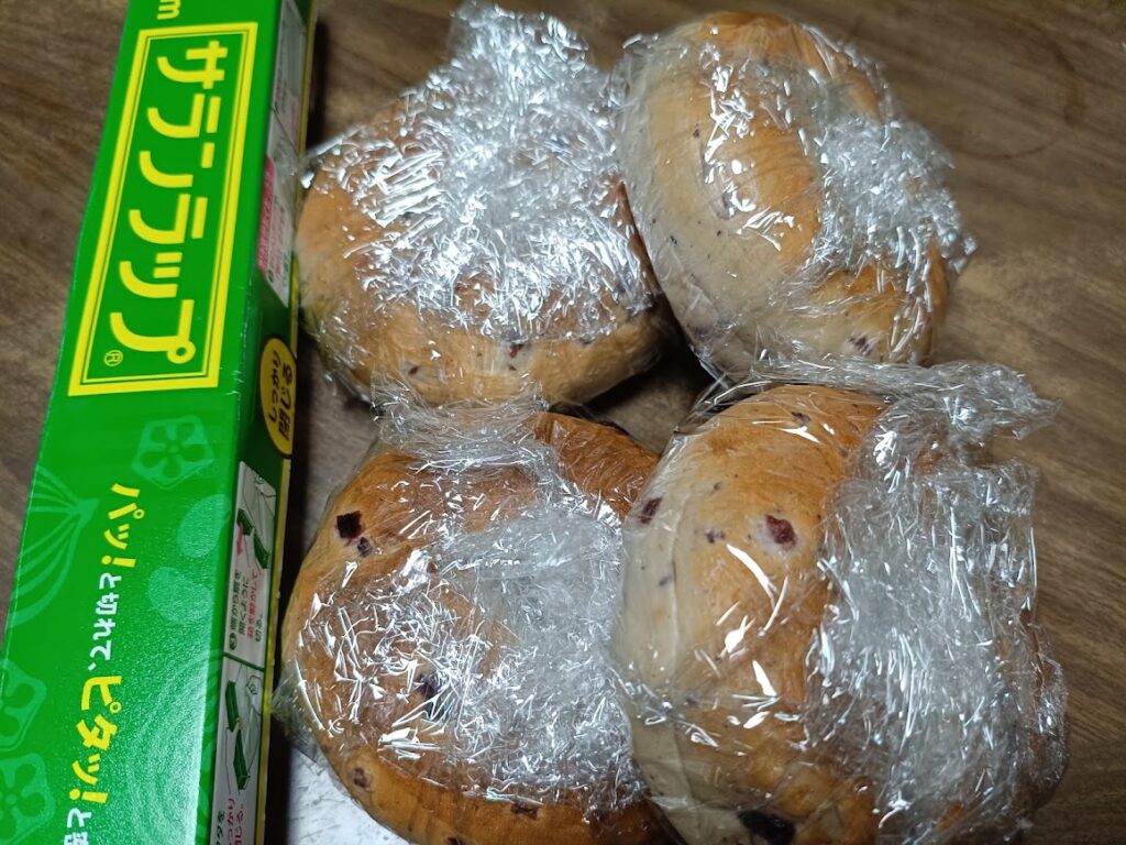 クランベリーブルーベリーベーグルを1個ずつラップで包んだ様子とサランラップの箱