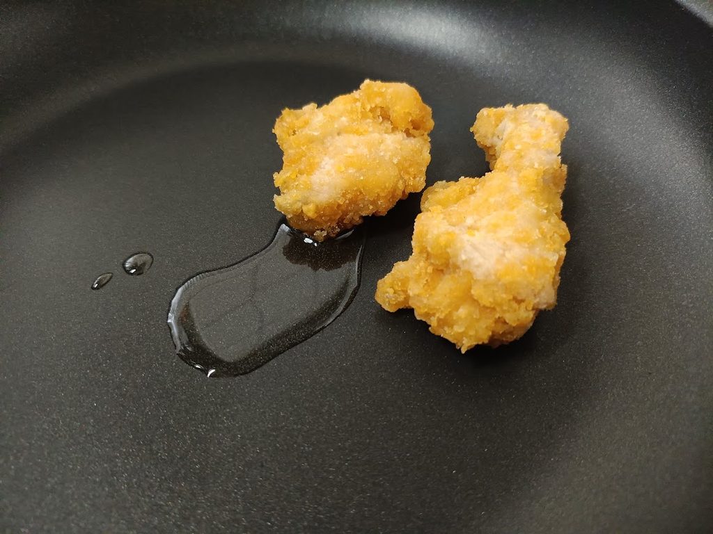 フライパンの油の横に置いた冷凍のままのバックリブのフライドチキン