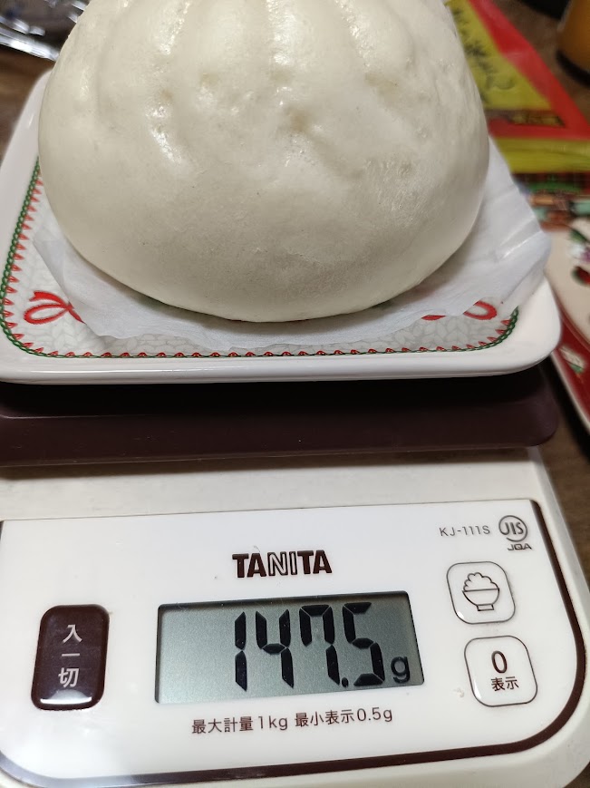 スケールで敷き紙込み147.5gと表示された金の肉まん