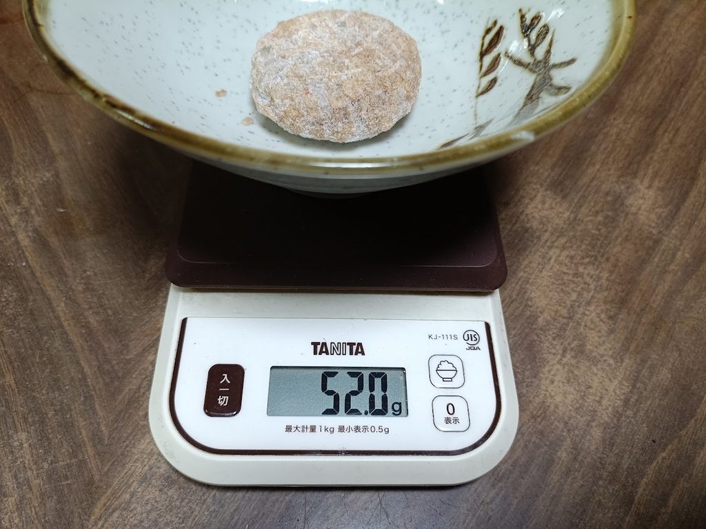 皿の上の冷凍のハンバーグ1個を、スケールで量っている様子(52.0g)