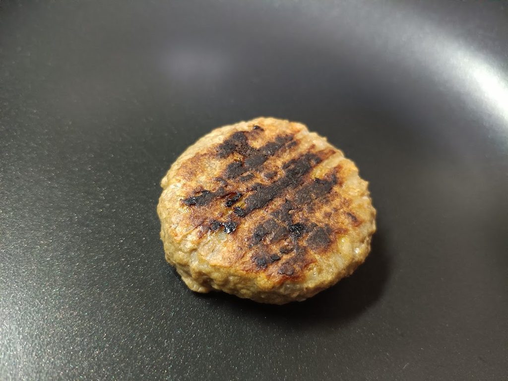 フライパンの上で焼いている、焼き目の付いたハンバーグ1個