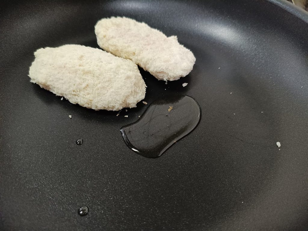 フライパンに入れた、冷凍のままのチキンカツ2枚と油
